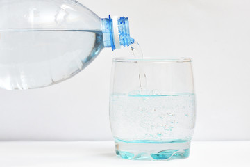 Beautiful and clean drinking water is poured into a transparent glass. Pouring water from bottle into glass on blue background