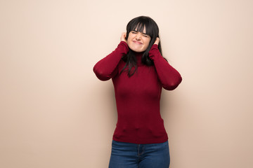 Young woman with red turtleneck covering ears with hands. Frustrated expression