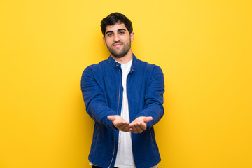 Fototapeta premium Man with blue jacket over yellow wall holding copyspace imaginary on the palm to insert an ad