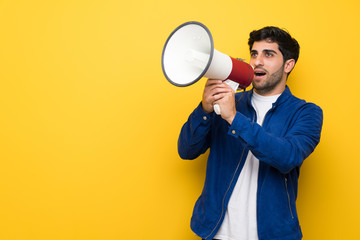 Man with blue jacket over yellow wall shouting through a megaphone