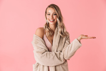 Pretty woman posing isolated over pink wall background dressed in fashion coat.