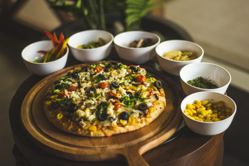 Italian fully loaded veg cheese Pizza on the table with toppings on the side