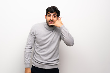 Young man over isolated white wall making phone gesture. Call me back sign