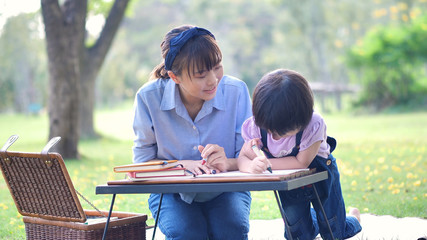 Asian family with Mother and daughter write on notebook. Happy enjoy having fun in nature or park and sunlight.