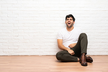 Young man sitting on the floor shouting to the front with mouth wide open