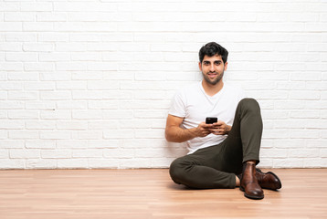 Young man sitting on the floor sending a message with the mobile