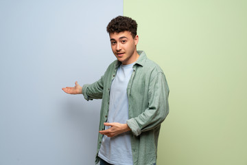 Young man over blue and green background pointing back and presenting a product