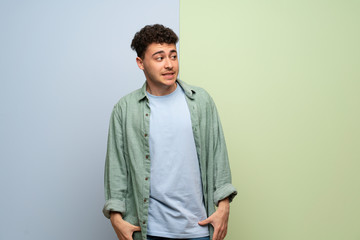 Young man over blue and green background is a little bit nervous and scared pressing the teeth
