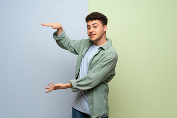 Young man over blue and green background holding copyspace to insert an ad