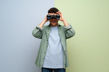 Young man over blue and green background and looking in the distance with binoculars