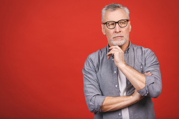 Portrait of a mature serious businessman wearing glasses isolated against red background. Happy senior man looking at camera with copy space. 