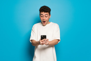 Young man over blue background surprised with a mobile