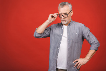 Portrait of a mature serious businessman with crossed hands wearing glasses isolated against red background. Senior man looking at camera with copy space. 