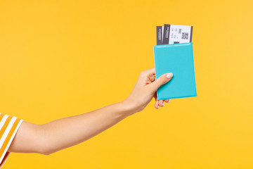Close-up shot of woman's hand holding passport with flight tickets or boarding pass isolated on yellow background