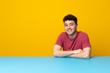 Young man with colorful wall and table keeping the arms crossed in frontal position