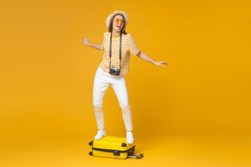 Dream about travel concept. Young funny female tourist standing on suitcase, pretending like she is surfing, isolated on yellow background