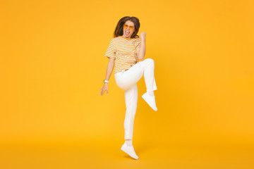 Active happy girl jumping in the air if she is a winner, isolated on yellow background