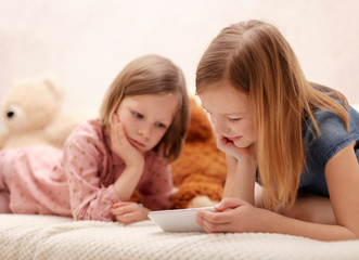 Two little girls (sisters 7 and 8 years old) are watching an e-book and a smartphone at home on the sofa with their cat.