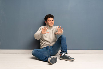 Young man sitting on the floor nervous stretching hands to the front