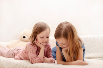 Two little girls (sisters 7 and 8 years old) are watching an e-book and a smartphone at home on the sofa with their cat.