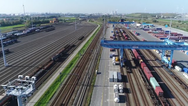 Aerial bird view of railroad container terminal with train loaded with containers by overhead crane also showing classification yard and heavy industry  in background 4k high resolution footage
