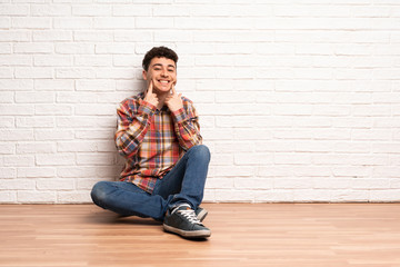 Young man sitting on the floor smiling with a happy and pleasant expression