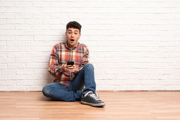 Young man sitting on the floor surprised and sending a message