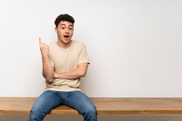 Young man sitting on table thinking an idea pointing the finger up