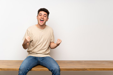 Fototapeta premium Young man sitting on table celebrating a victory in winner position