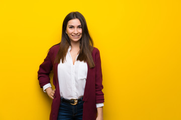 Young woman over yellow wall posing with arms at hip and smiling