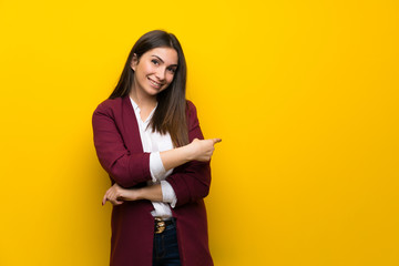 Young woman over yellow wall pointing back