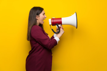 Young woman over yellow wall shouting through a megaphone