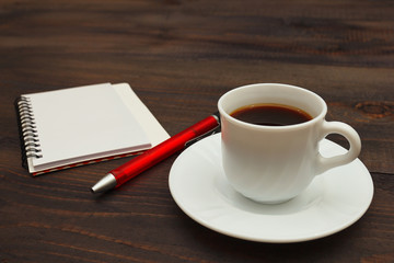 Cup of espresso, pen and notebook on a wooden background