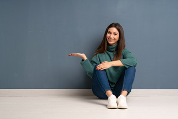 Young woman sitting on the floor holding copyspace imaginary on the palm to insert an ad