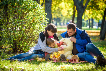 Fototapeta premium happy family enjoying autumn picnic. Father mother and son sit on field with apples basket teddy bear and reading book. Happy family leisure together concept