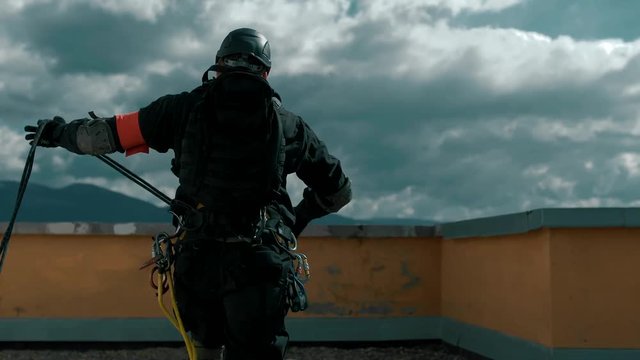 Rescuer industrial climber runs along the roof to the edge to go down to the burning apartment and save people