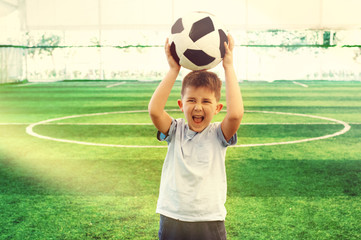 Portrait of a young soccer player school kid at football field shouting and raising ball over his head