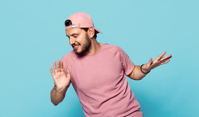 Young cheerful bearded man in stylish clothes and pink baseball cap dancing happily on blue background