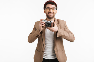 Photo of smiling man 30s wearing hipster hat rejoicing while holding and photographing on retro camera