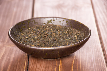Lot of pieces of dry black tea earl grey in a grey ceramic bowl on brown wood