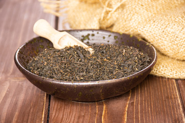 Lot of pieces of dry black tea earl grey in a grey ceramic bowl with wooden scoop on jute cloth on brown wood