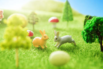 Little Easter bunny toys and Easter eggs on a green grass. Yellow easter egg spring meadow with two white rabbit and easter eggs. Fairy tale
