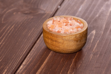 Lot of pieces of pink himalayan salt crystals in a wooden bowl on brown wood