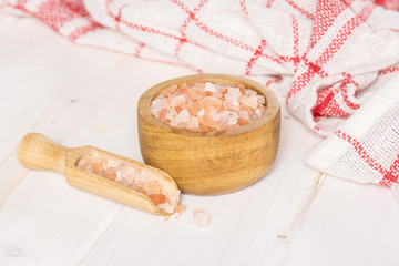 Lot of pieces of mineral pink himalayan salt crystals in a wooden bowl on white wood