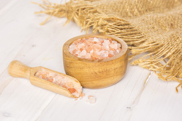 Lot of pieces of pink himalayan salt crystals in a wooden bowl on white wood
