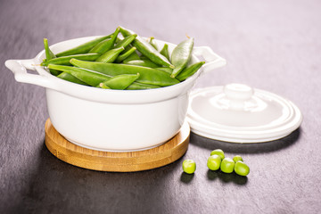 Lot of whole green sugar snap pea pods with a stewpan on grey stone