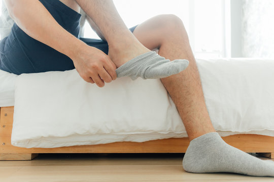 Man is wearing socks into his feet in the bedroom. Concept of getting ready and dress up.