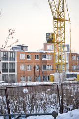 Abandoned construction of a multi-storey building. Tower crane, and a house with broken glass. Winter. Russia