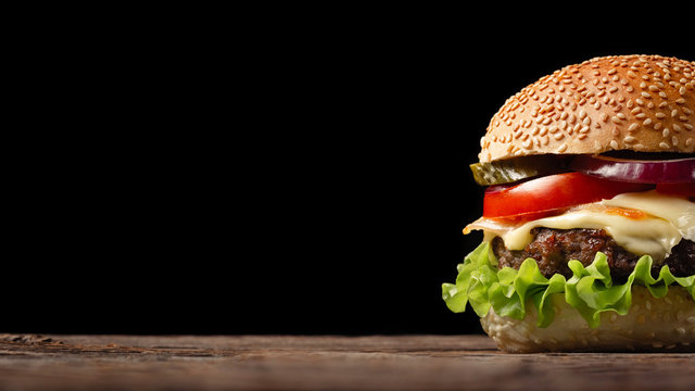 Homemade hamburger close-up with beef, tomato, lettuce, cheese and onion on wooden table. Fastfood on dark background