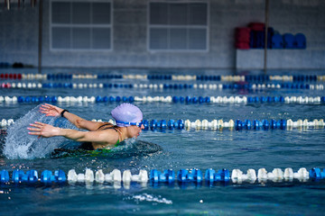 Female athlete swims with a butterfly style. Splashes of water scatter in different directions.